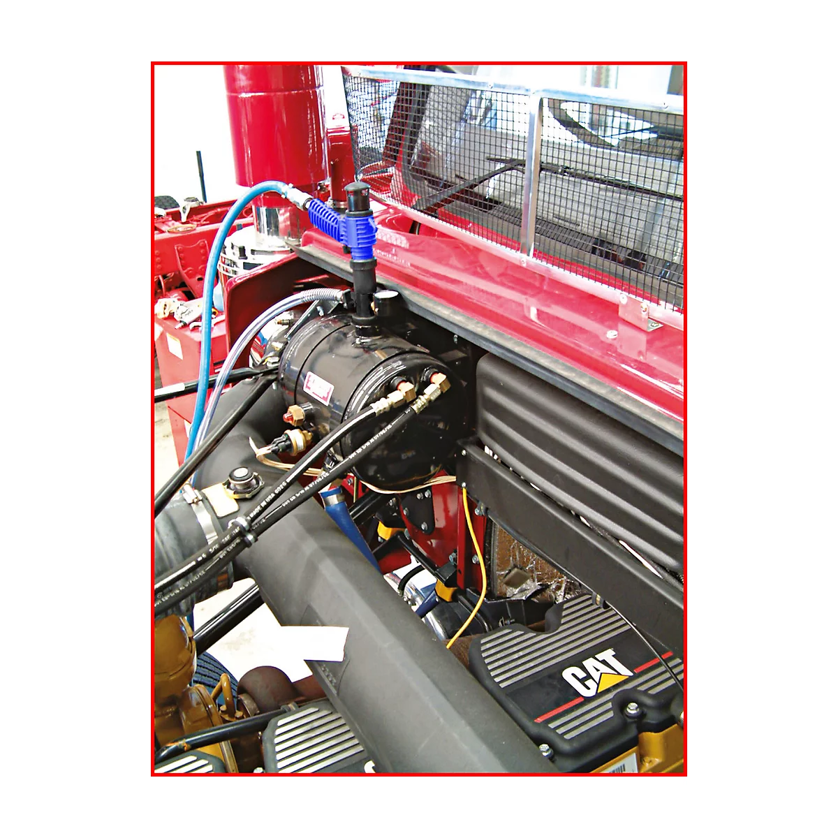 Motor eines Lastwagens. Schwarze Teile, blaue Schläuche, gelbe Kabel, und Schriftzug CAT. Roter Rahmen.